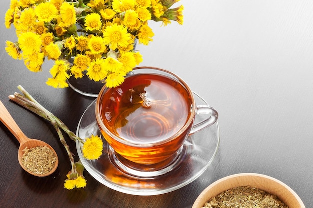 Healthy tea closeup bucket with coltsfoot flowers and mortar on dark table herbal medicine