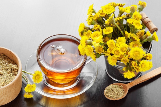 Healthy tea in glass cup closeup bucket with coltsfoot flowers and mortar