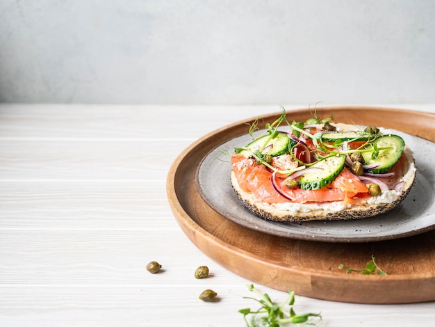 Healthy toast with cream cheese, salmon, fresh cucumber, capers, red onion, black pepper and pea sprouts on plate.