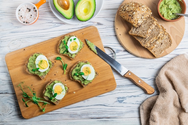 Healthy toasts with whole grain bread, avocado and boiled egg on wooden board