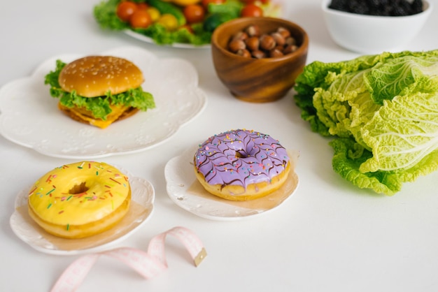 Healthy or unhealthy food Conceptual photo of healthy and unhealthy food with measuring tape Fruits and vegetables vs donuts sweets and burgers