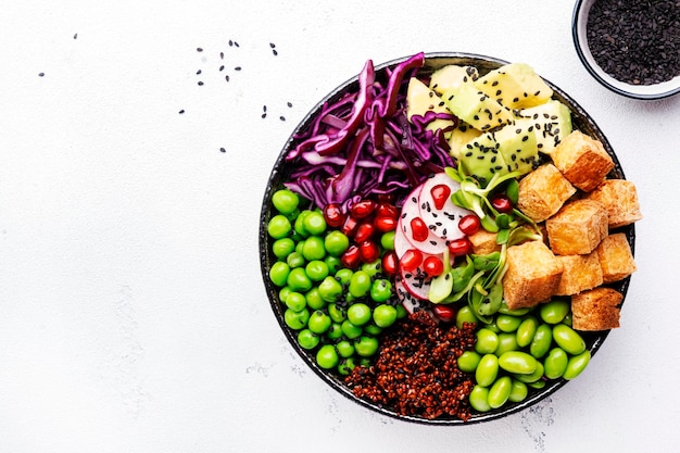 Healthy vegan diet food Buddha bowl with quinoa fried tofu avocado edamame beans peas radish red cabbage and sesame seeds White kitchen table background top view