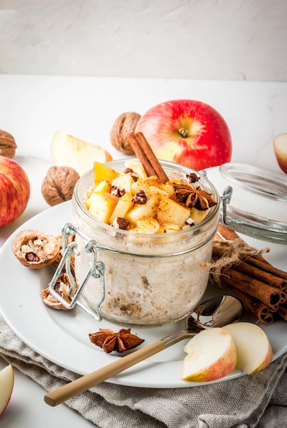 Healthy vegan food Dietary breakfast or snack Apple pie overnight oats with apples yogurt cinnamon spices walnuts In a glass on a white marble table