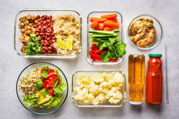 Healthy vegan food in glass containers, top view. Rice, beans, vegetables, hummus and juice. 