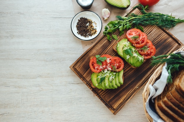 Healthy vegan homemade sandwich, avocado and tomatoes with dark grain bread on a wooden board.