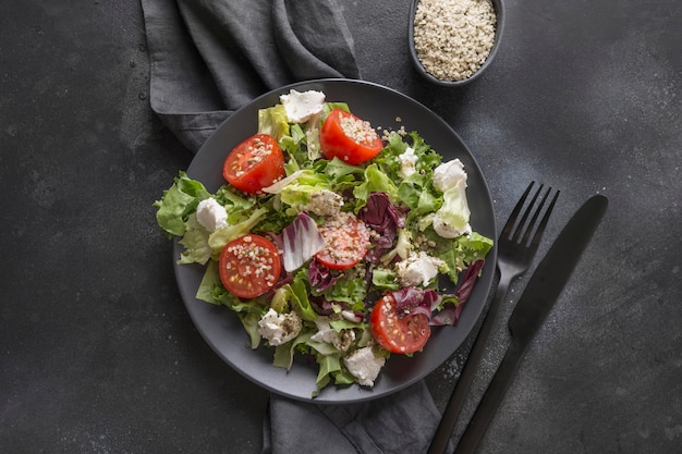 Photo healthy vegan salad in black dish with fresh tomato, greens, seeds hemp for clean eating. top view.