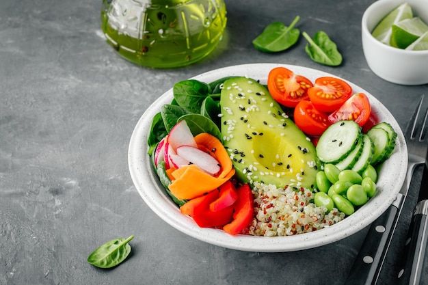 Healthy vegetable lunch Buddha bowl Avocado quinoa tomatoes cucumbers radishes spinach carrots red paprika and edamame beans salad