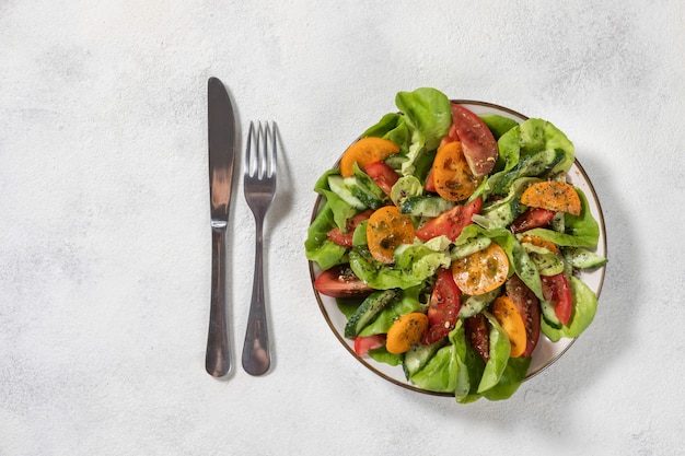 Healthy vegetable salad from fresh vegetables of tomatoes, cucumbers, onions, spinach, lettuce on a plate. Diet menu. View from above.