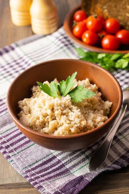 Healthy vegetarian breakfast with wheat porridge in a bowl, bread, tomatoes and parsley