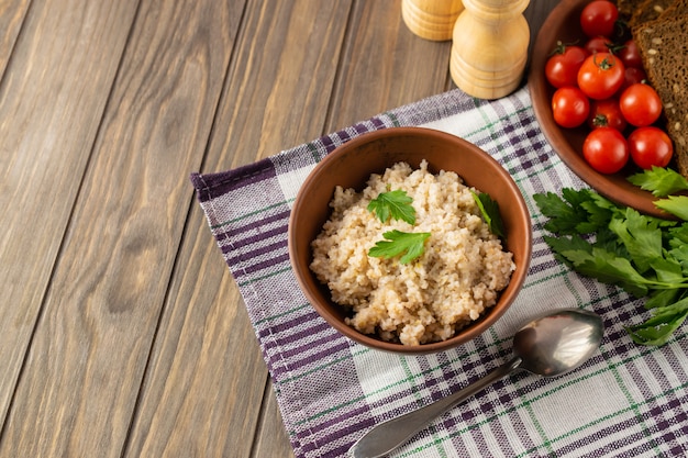 Healthy vegetarian breakfast with wheat porridge in a bowl, bread, tomatoes and parsley