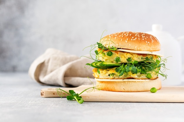 Healthy Vegetarian burger with egg and pea shoots and seeds microgreen, fresh salad, cucumber slice on a cutting wooden board on light background. Selective focus