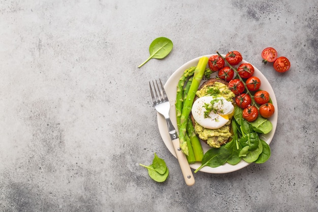 Healthy vegetarian meal plate. Toast, avocado, poached egg, asparagus, baked tomatoes, spinach.