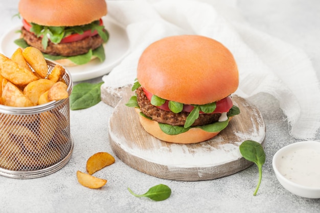 Healthy vegetarian meat free burgers on round chopping board with vegetables on light background with potato wedges