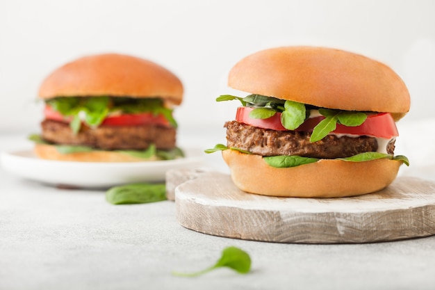 Healthy vegetarian meat free burgers on round chopping board with vegetables and spinach on light background.