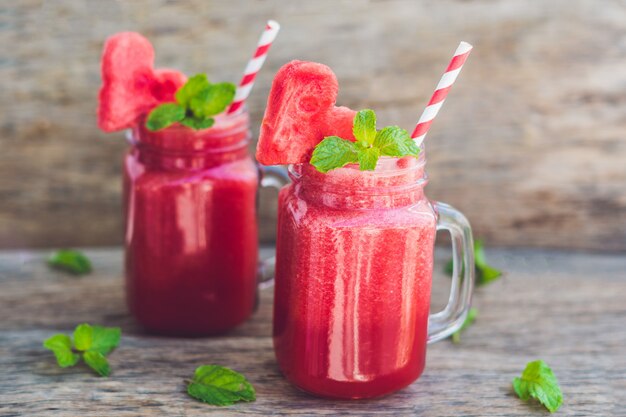 Healthy watermelon smoothie in Mason jars with mint and striped straws on a wood table