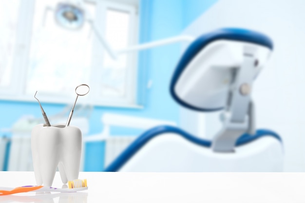 Healthy white tooth and dentist mirror with explorer probe instrument near toothbrush against blurred dentist Office background.