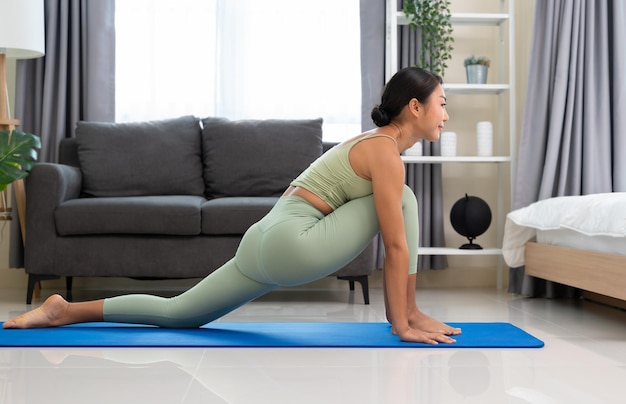 Healthy woman in green top and leggings stretching in Low Lunge pose at home