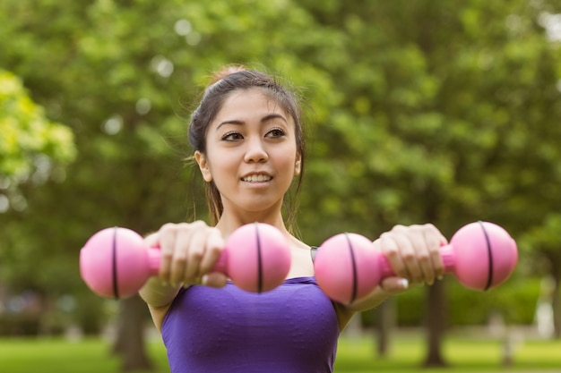 Healthy woman lifting dumbbells in park