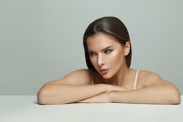 Photo healthy woman sitting on white table and looking away on white background