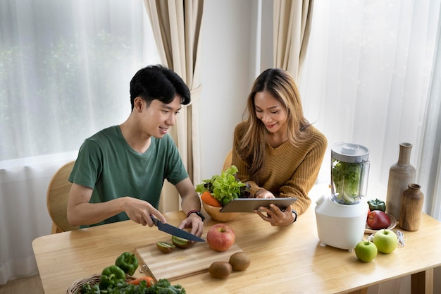 Healthy young couple preparing ingredients for making green vegetables detox smoothie in kitchen