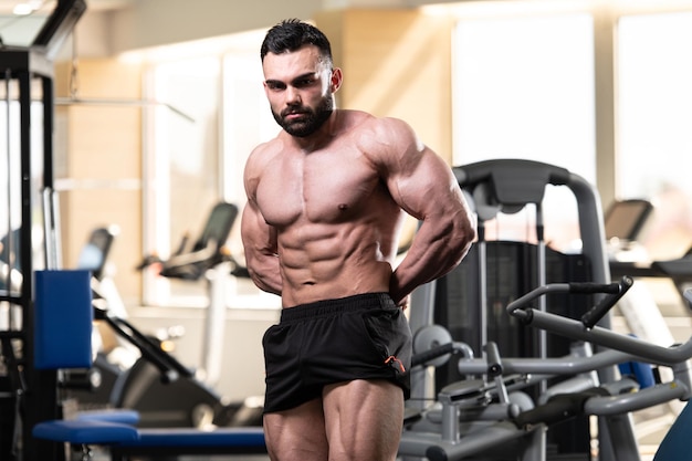 Healthy Young Man Standing Strong In The Gym And Flexing Muscles Muscular Athletic Bodybuilder Fitness Model Posing After Exercises