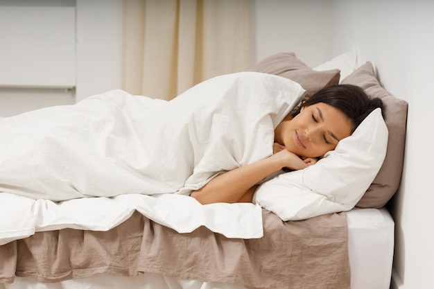 Healthy young woman covers blanket sleeping with closed eyes on bed in bedroom