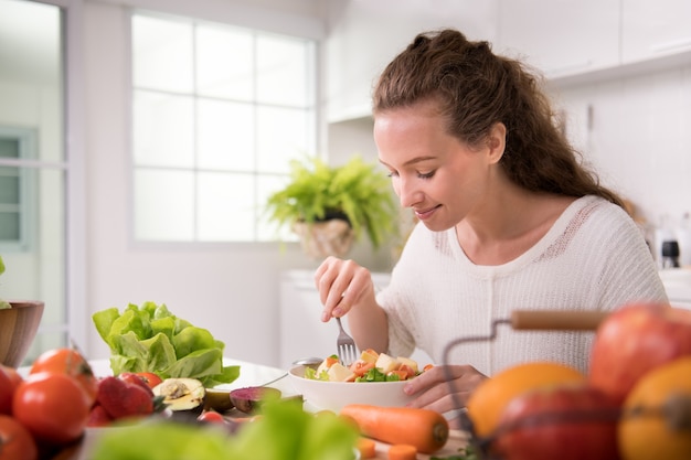 Healthy young woman eating salad in the kitchen