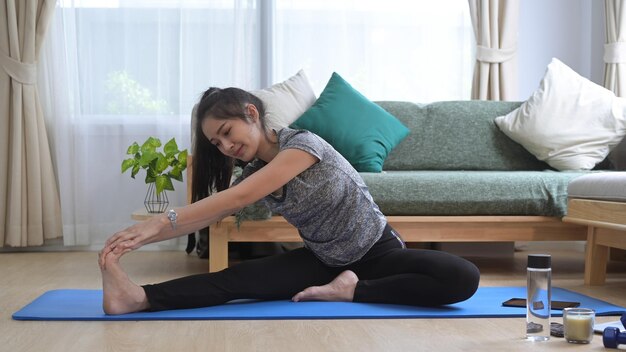 Healthy young woman sitting in mat warming up stretching before workout at home