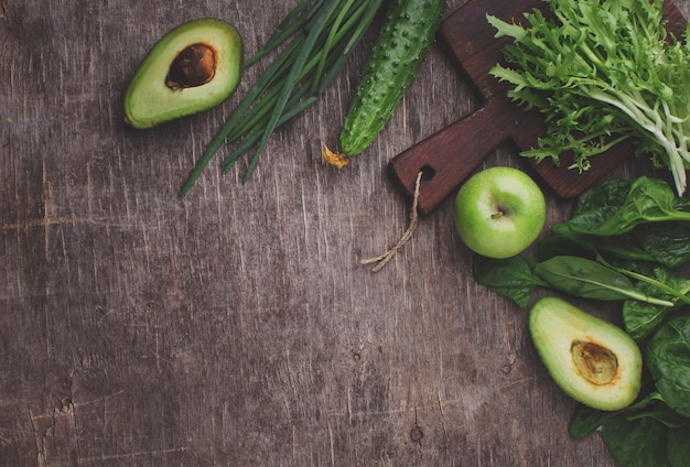 Healty green vegetable: spinach, cucumber, lettuce, apple and avocado on dark background. flat lay, copy space.