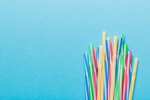 Heap of colorful plastic drinking straws on Colored background flat lay Copy Space for text