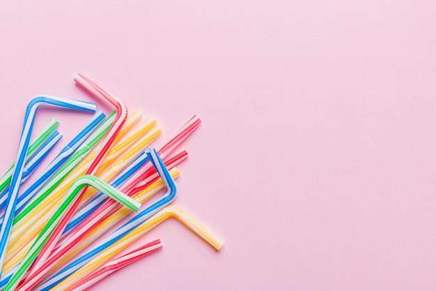 Heap of colorful plastic drinking straws on Colored background flat lay Copy Space for text