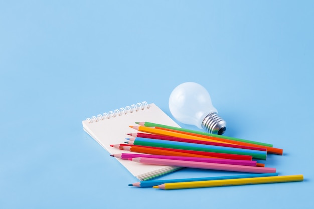 Heap of colour pencils and light bulb on blue surface