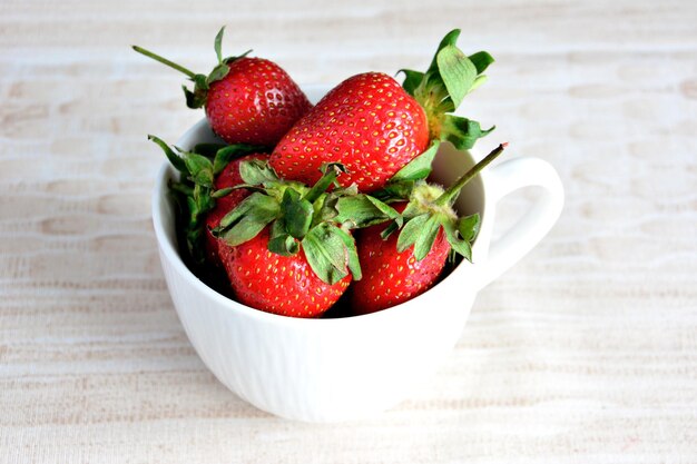 heap of fresh garden strawberries isolated in white cup on beige background, macro