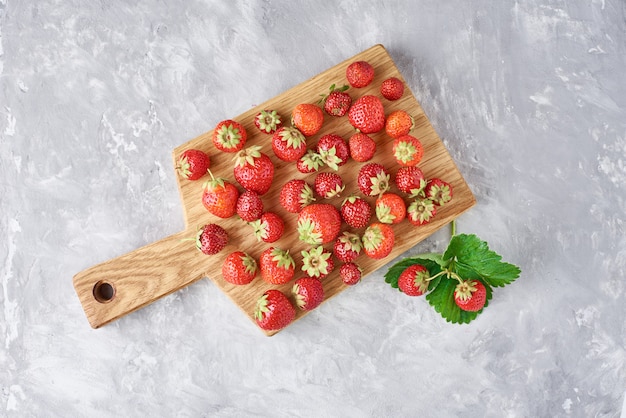 Heap of fresh strawberries with cutting board on a gray, top view. Healthy nutrition