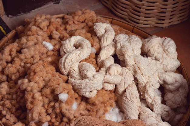 Heap of natural cotton yarn on white and brown raw cotton buds in basket