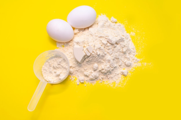 Photo heap of protein powder with plastic spoon and two egg on yellow background