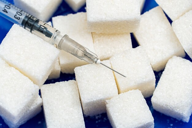 Heap of sugar and syringe on blue background. Testing, treatment diabetes concept