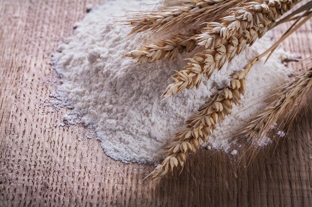 Heap of white flour with ears of wheat and rye on wooden board