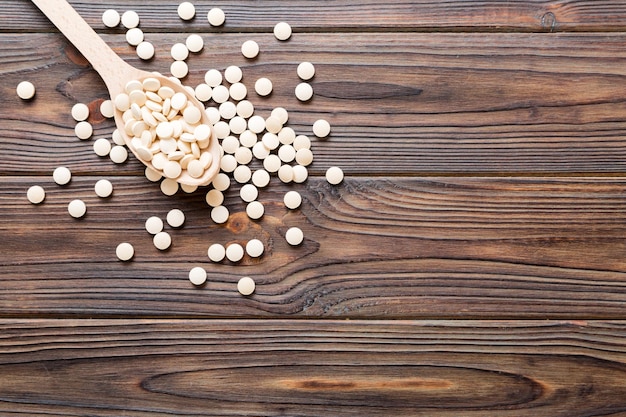 Heap of white pills on colored background Tablets scattered on a table Pile of red soft gelatin capsule Vitamins and dietary supplements concept