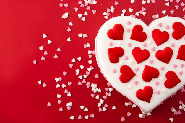 Heart cake for St. Valentine's Day,  decorated with sugar hearts on red background