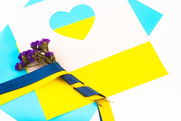 Heart cut out of paper and painted in blue and yellow colors and flowers in ribbon of flag