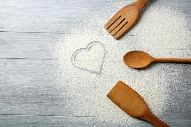 Heart of flour and kitchen utensils on wooden background