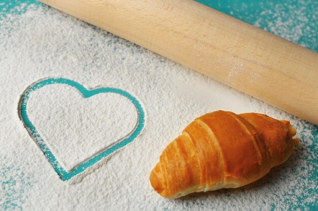 Photo heart of flour and rolling pin on color wooden background