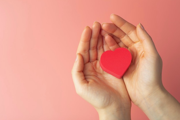 Heart in the hands of a female on a colored background. Background for Valentine's Day (February 14) and love.