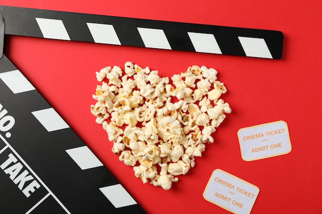 Heart laid out from popcorn, clapperboard and tickets on red background