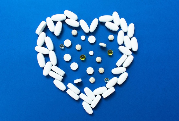 Heart laid out of pills and capsules on a blue background  Concept of heart disease