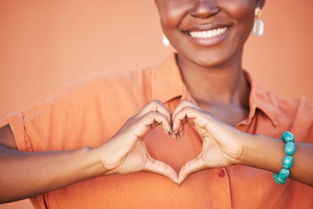 Heart love and black woman hands for beauty african self care and fashion cosmetics with peace happiness and smile with teeth Summer orange wall background and happy woman with self love sign