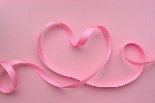 Heart made of pink ribbon on a pink background