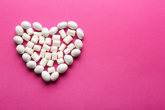 Heart made of white candies and marshmallows on pink