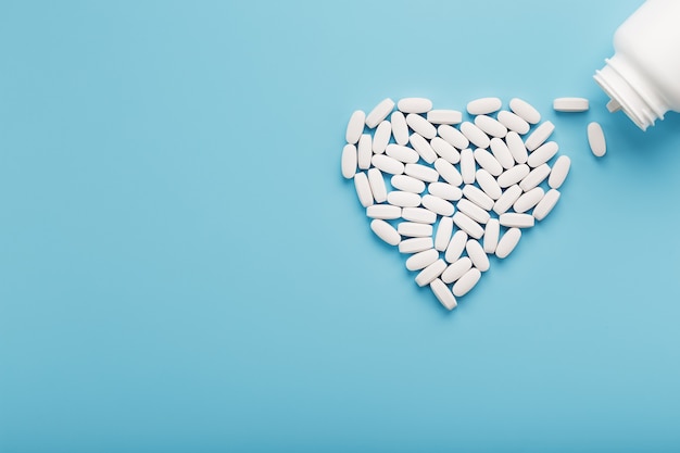 Heart made of white pills from a bottle on a blue background. Vitamins for health. Place for text